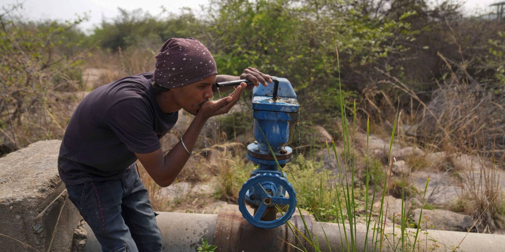 In Indien trinkt ein Mann Wasser aus einer undichten Wasserstelle.