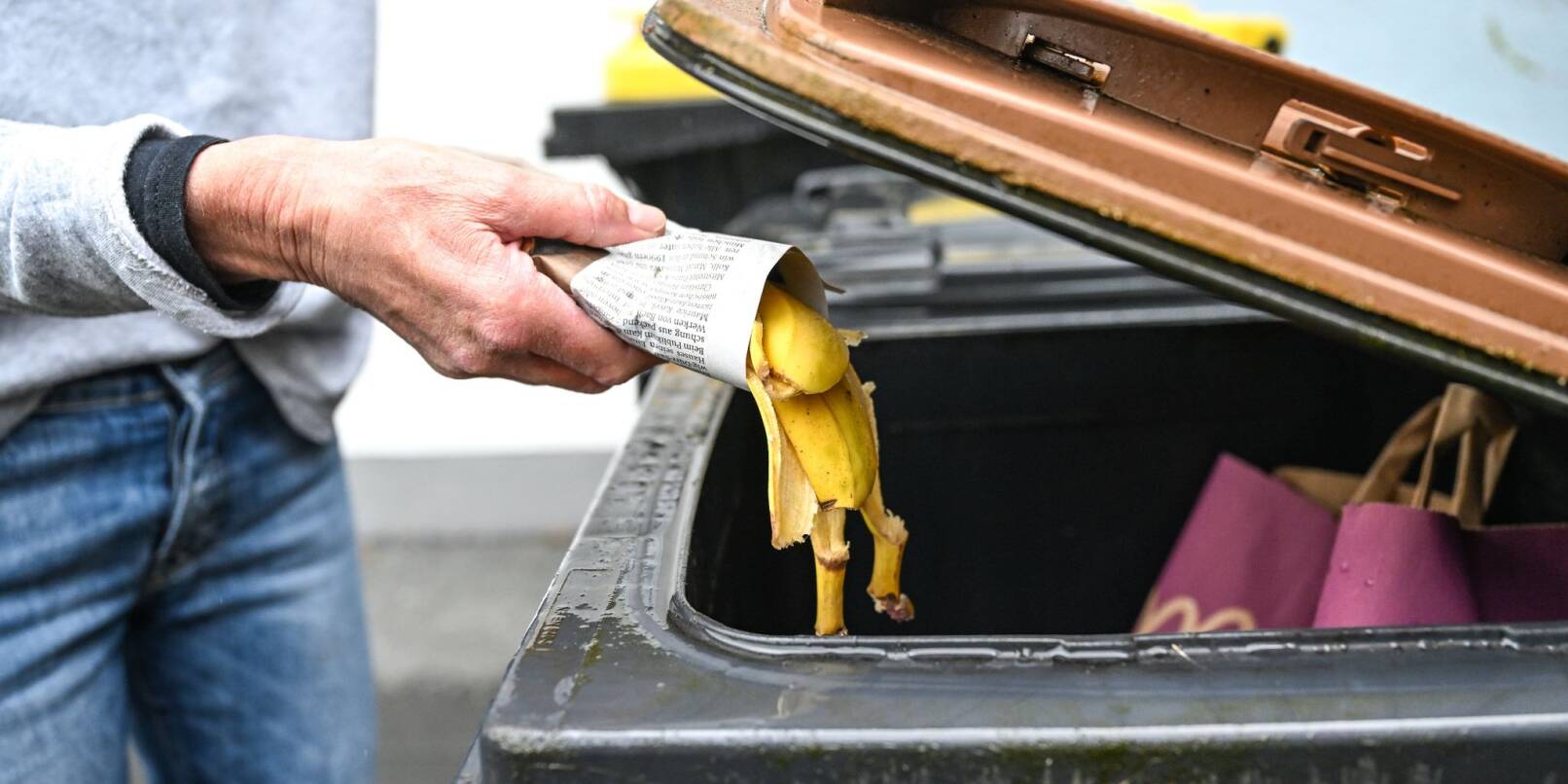 Eine Frau wirft in Zeitungspapier gewickelte Bananenschalen in eine Mülltonne für den Biomüll.