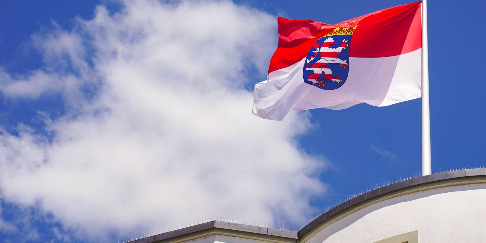 Die hessische Landesfahne weht auf dem Dach des hessischen Landtages vor dem Sommerhimmel.