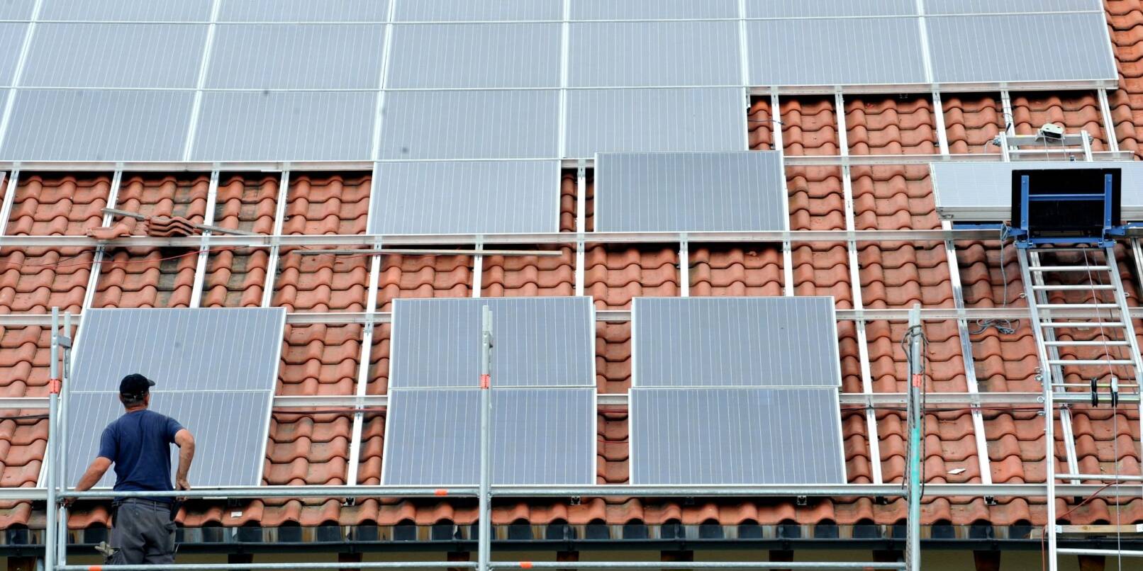 Ein Arbeiter installiert auf einem Dach eine Solaranlage. Ein Arbeiter installiert auf einem Dach eine Solaranlage.