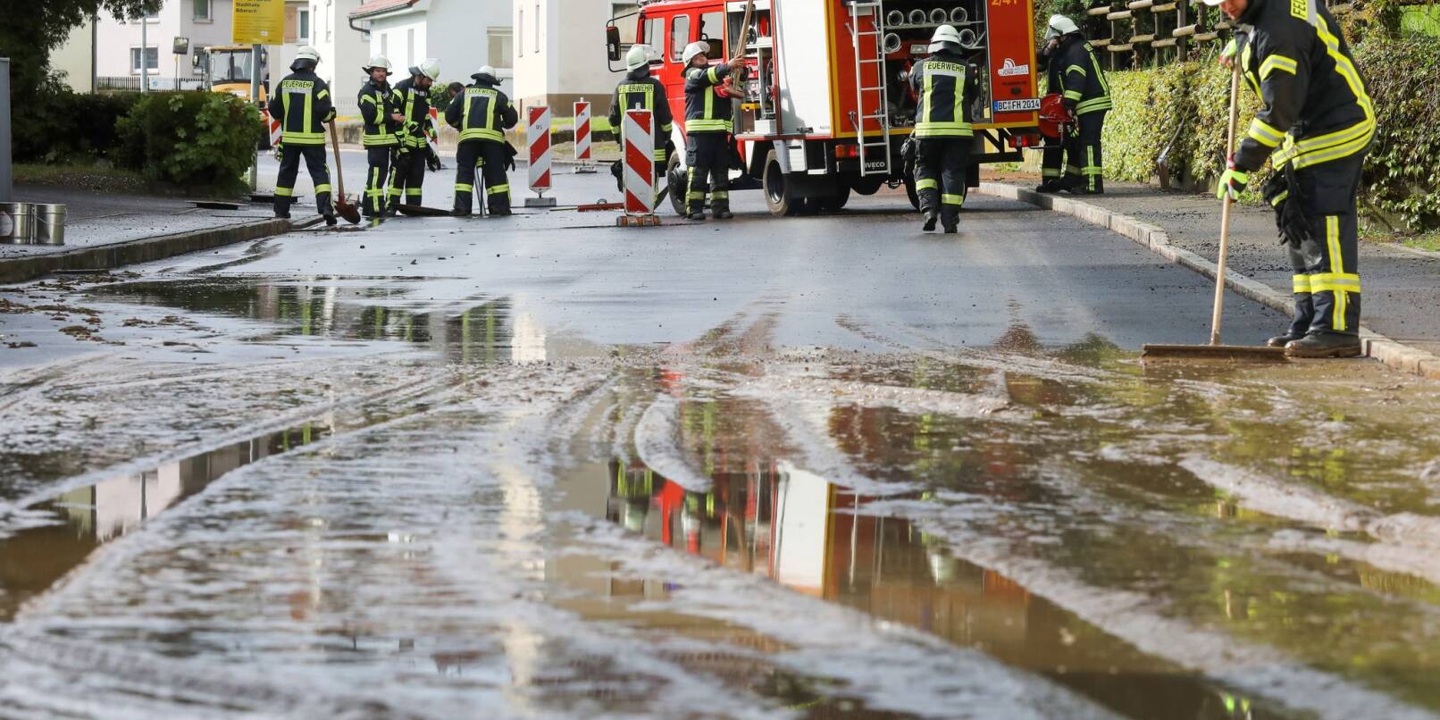 Einsatzkräfte der Feuerwehr reinigen eine überflutete und verschmutzte Straße.