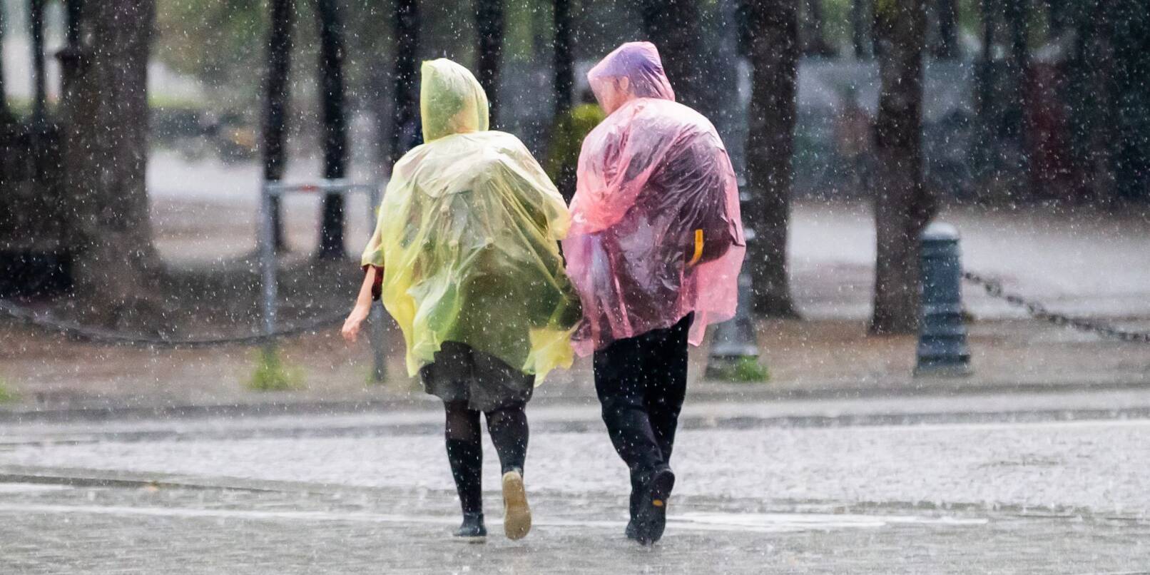 Menschen mit Plastik-Regenschutz gehen durch den Regen.