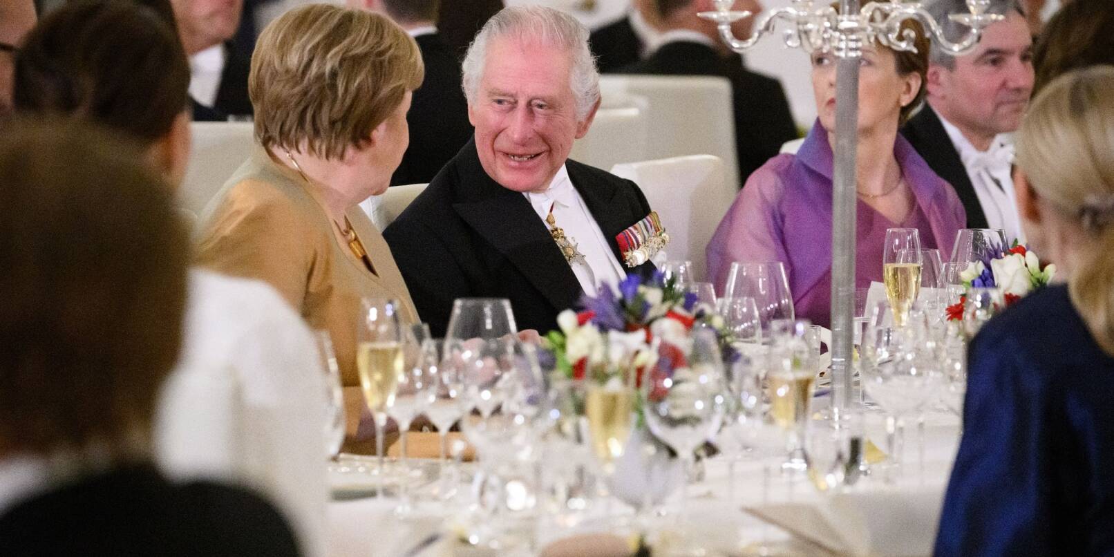 Unter den 130 geladenen Gästen im Schloss Bellevue ist auch Ex-Bundeskanzlerin Angela Merkel, die sich angeregt mit König Charles unterhält.