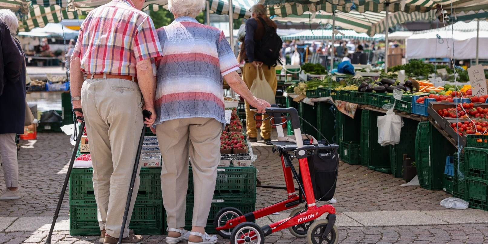 Zwei Senioren stehen mit Gehhilfen und Rollator auf dem Wochenmarkt in der Leipziger Innenstadt.