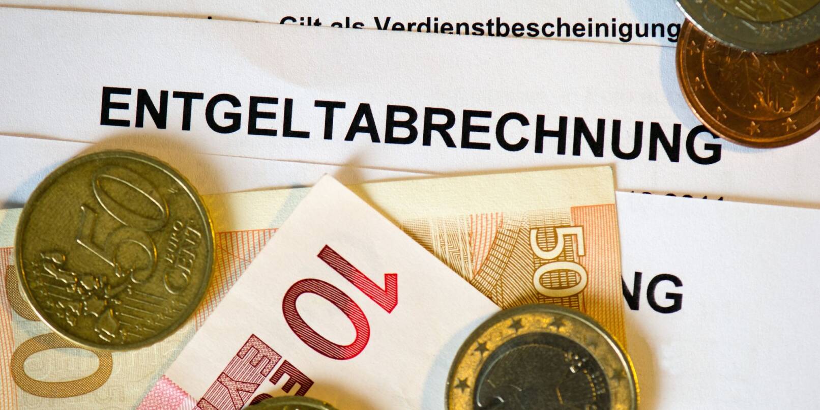 Auf Lohn- und Gehaltsabrechnungen (Entgeltabrechnungen) liegen Euromünzen und Eurogeldscheine.
