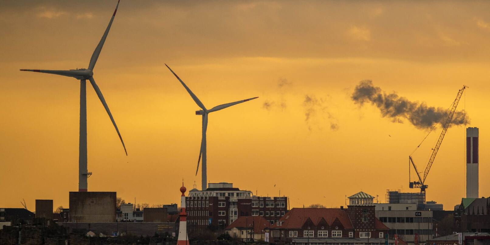 Zwei Windräder zeichnen sich vor dem morgendlichen Himmel in Bremerhaven ab.