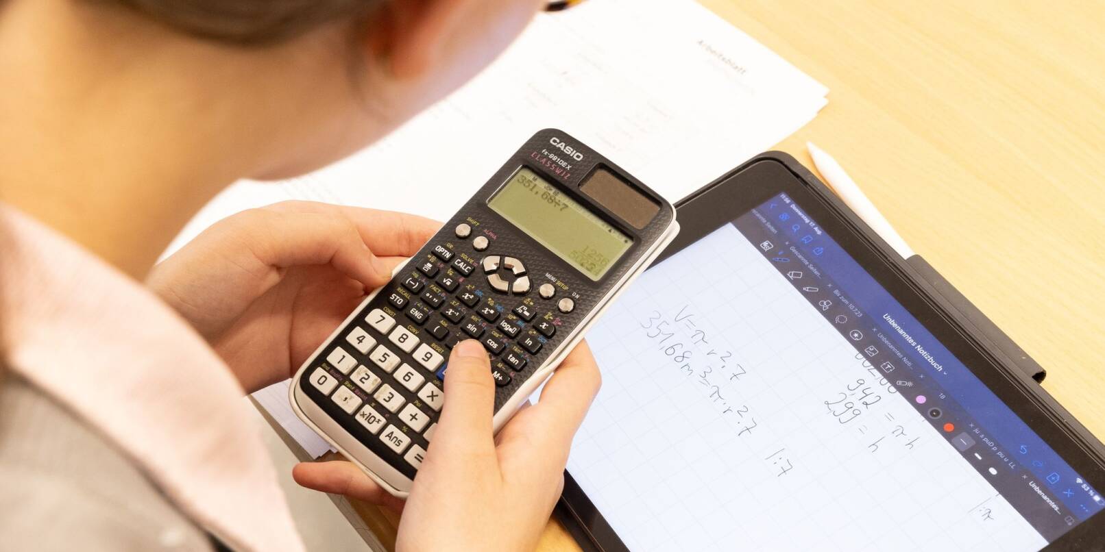 Eine Schülerin löst auf einem Taschenrechner und einem iPad eine Rechenaufgabe.