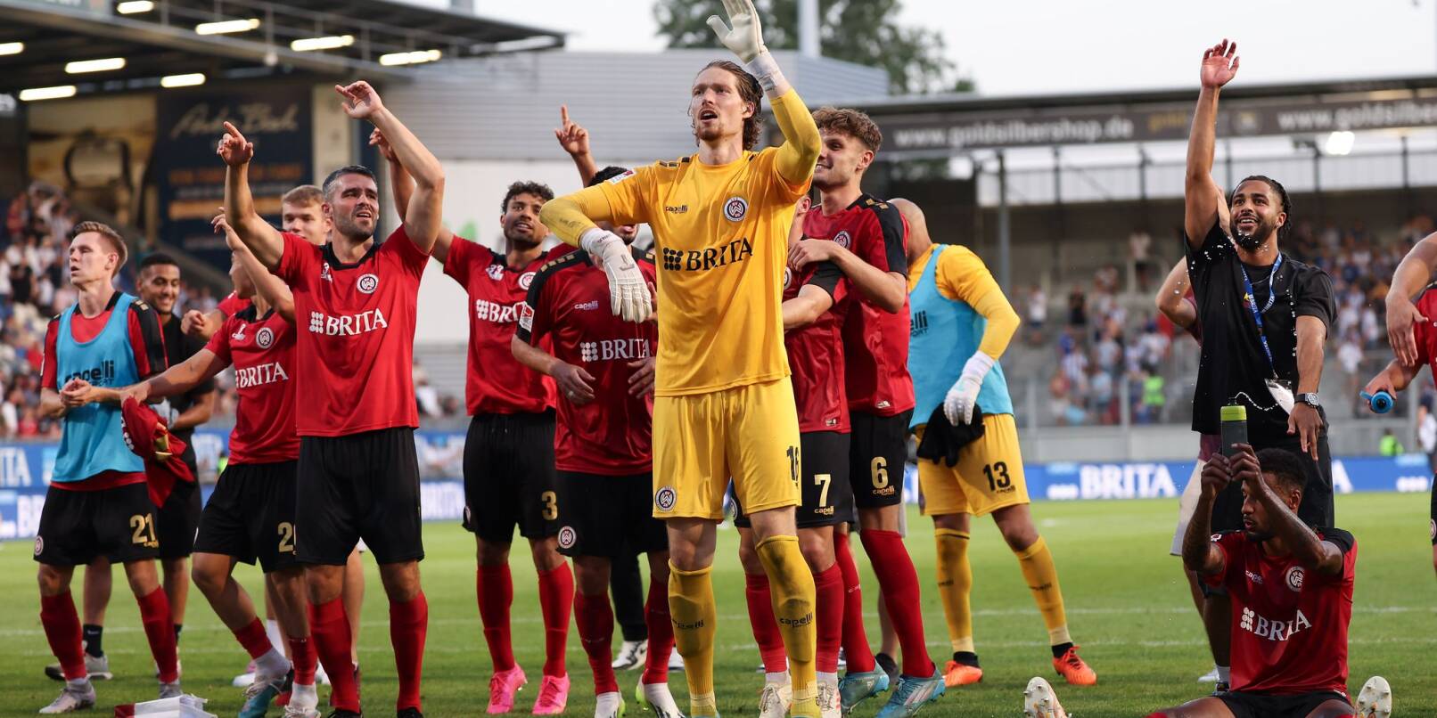 Torwart Florian Stritzel (M) vom SV Wehen Wiesbaden und seine Teamkollegen feiern nach dem Schlusspfiff gemeinsam mit den Fans.