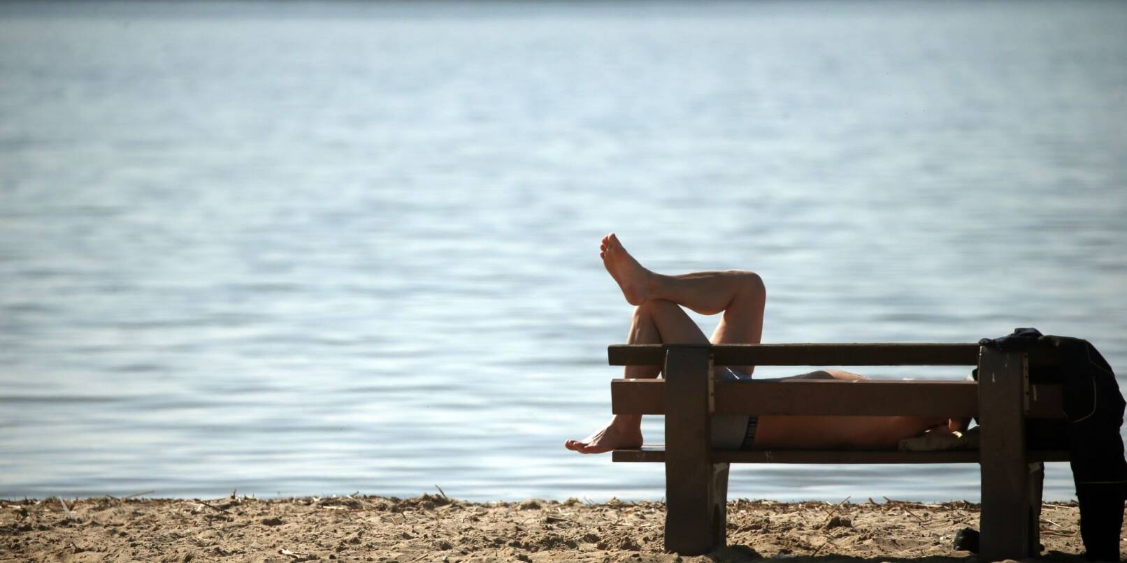 Ein Mann liegt in einem Strandbad auf einer Bank.