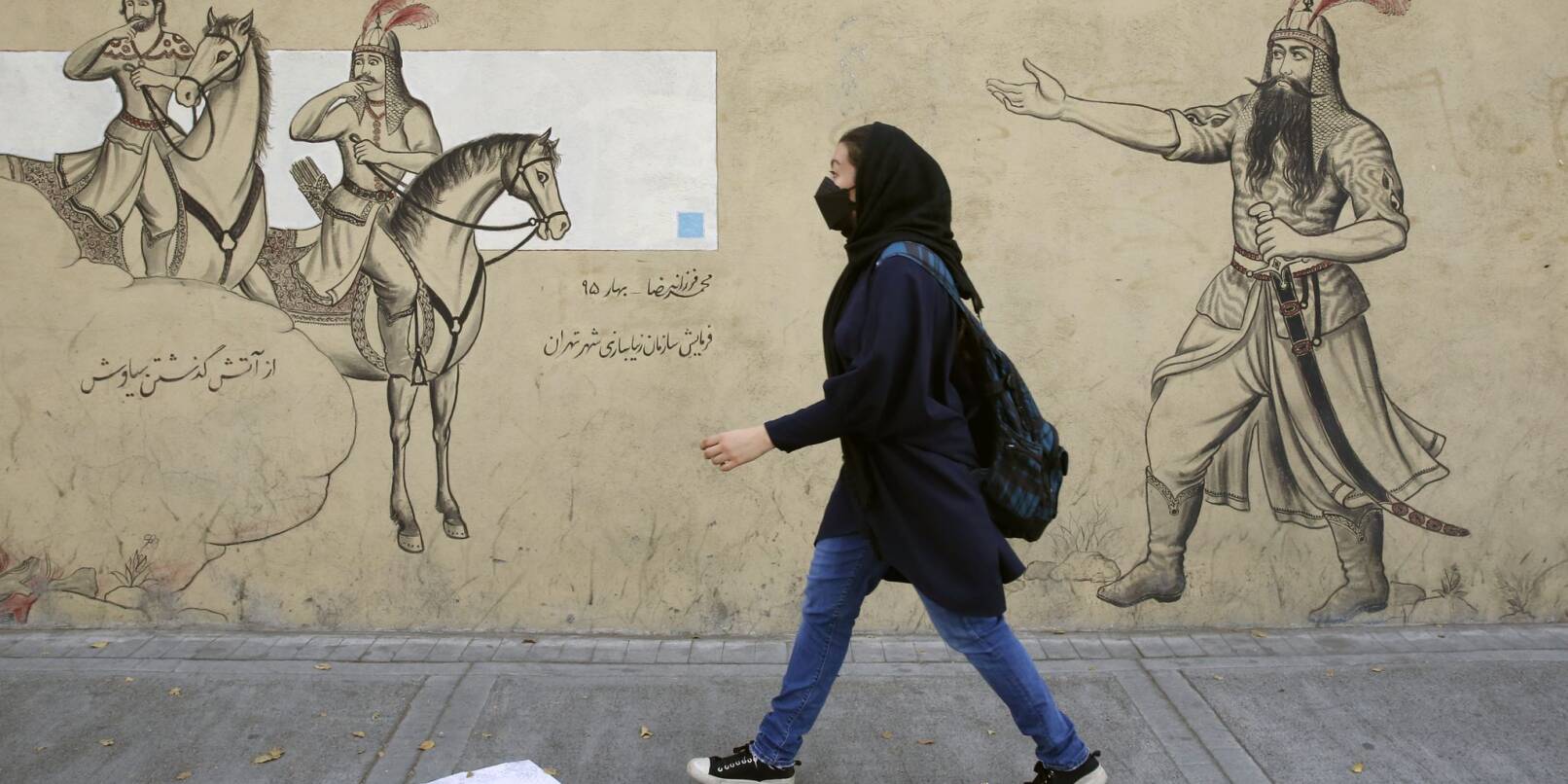 Ein Mädchen geht an einer Häuserfassade in Teheran entlang.