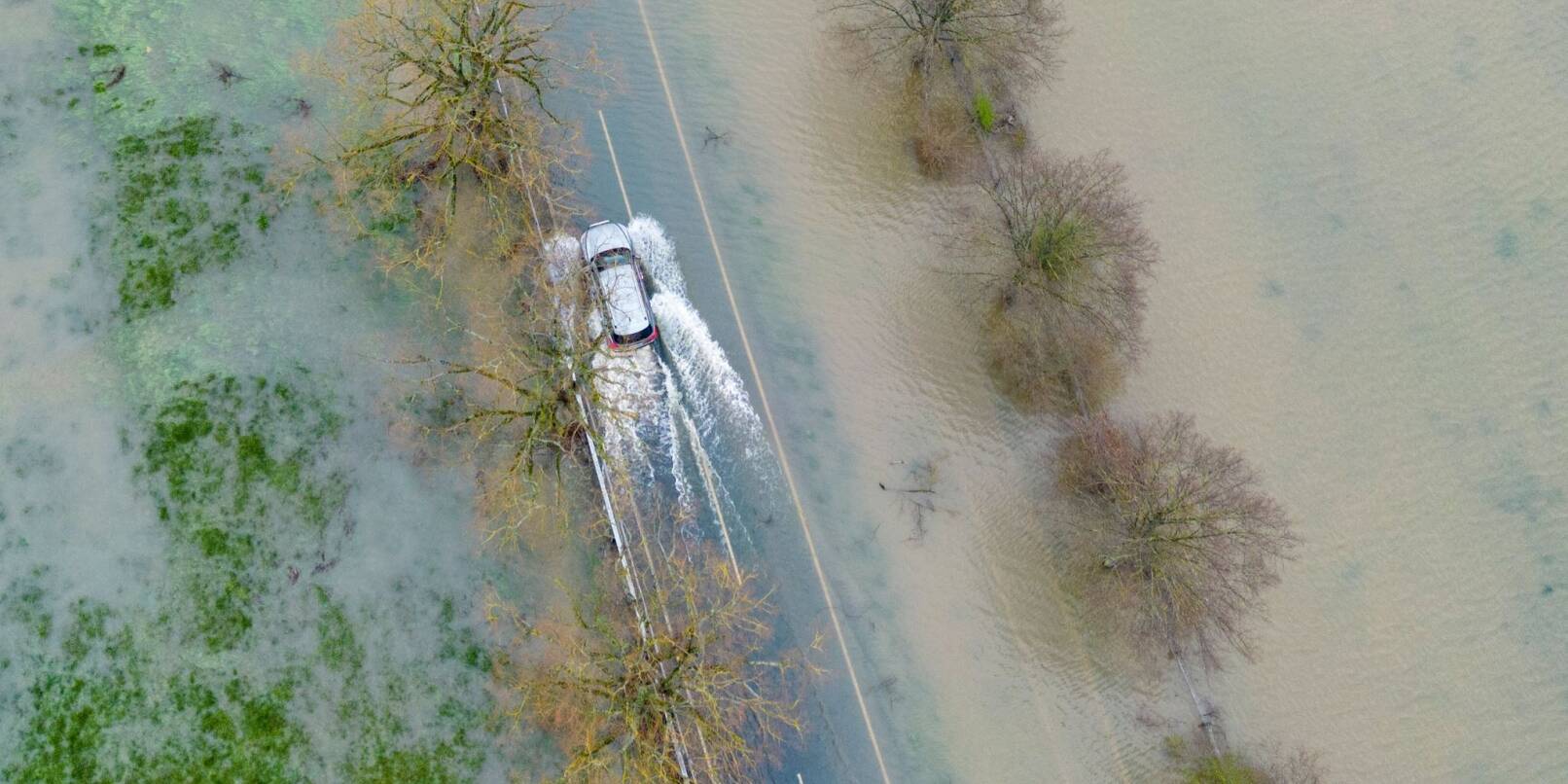 Ein Auto fährt über eine vom Hochwasser überflutete Landstraße in Mittelhessen.