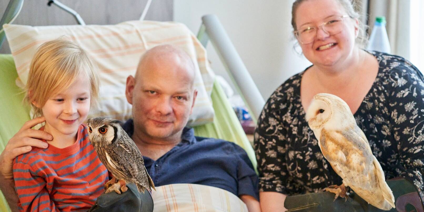 Swen Pinkatschek (M), der an einem Hirntumor leidet, freut sich mit seiner Frau Tamara und seinem Sohn Claas (7) über den Besuch von Schleiereule Emma und Weißgesichtseule Merlin.