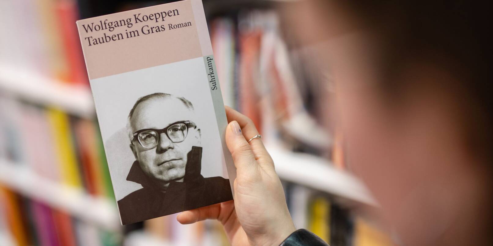Eine Frau hält in einer Buchhandlung das Buch «„Tauben im Gras»“ von Wolfgang Koeppen in ihrer Hand.