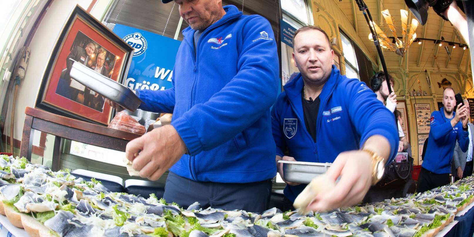 Axel Schulz, ehemalige Profiboxer (l-r), und André Domke, Fischsommelier und -händler, belegen das gigantische Fischbrötchen mit Salat, Fisch und Zwiebeln.