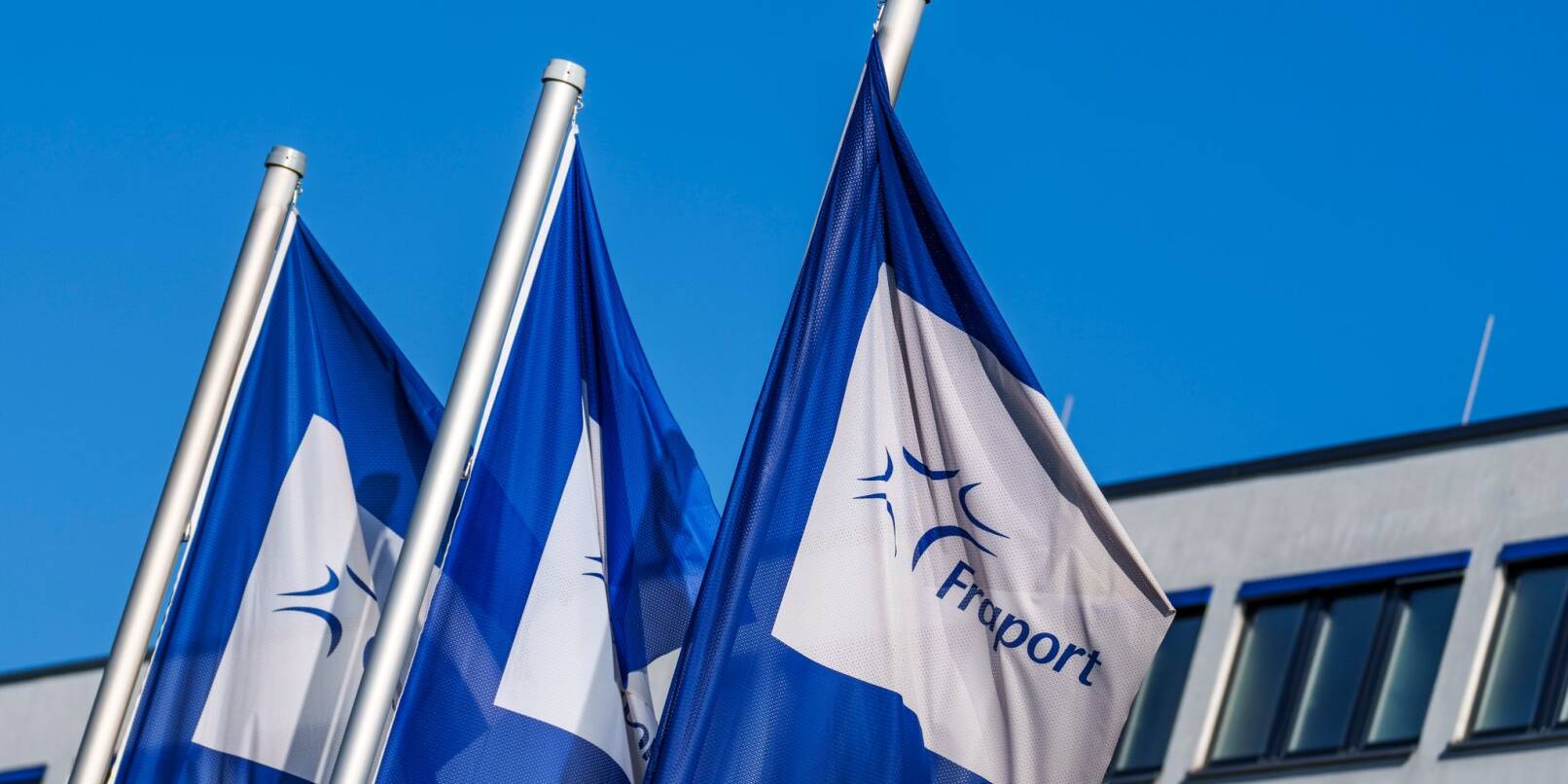 Flaggen mit dem Logo der Fraport AG wehen vor der Firmenzentrale im Wind.