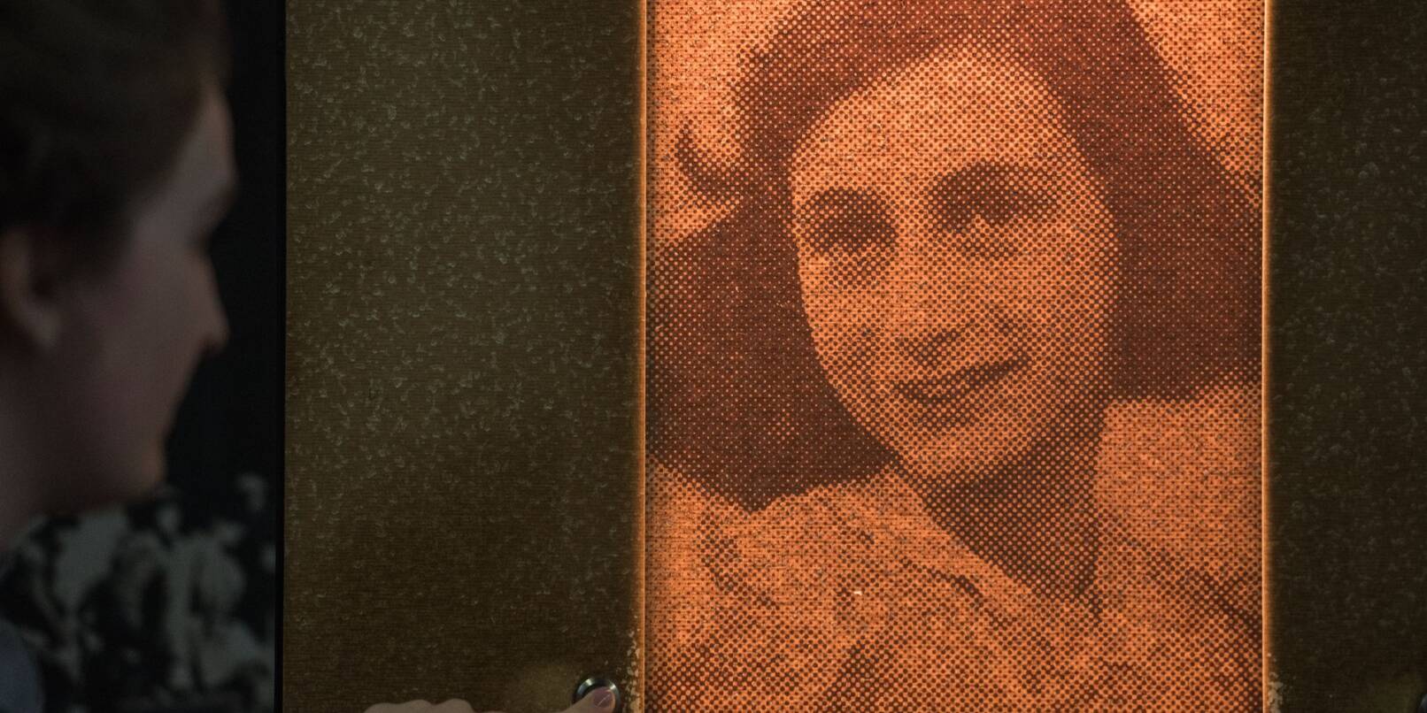 Eine Besucherin beleuchtet durch Knopfdruck ein Porträt der Anne Frank.