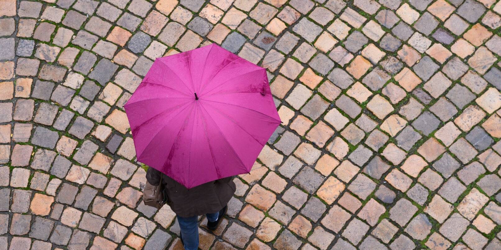 Eine Frau geht mit einem Regenschirm auf einer Straße entlang. Eine Frau geht mit einem Regenschirm auf einer Straße entlang.