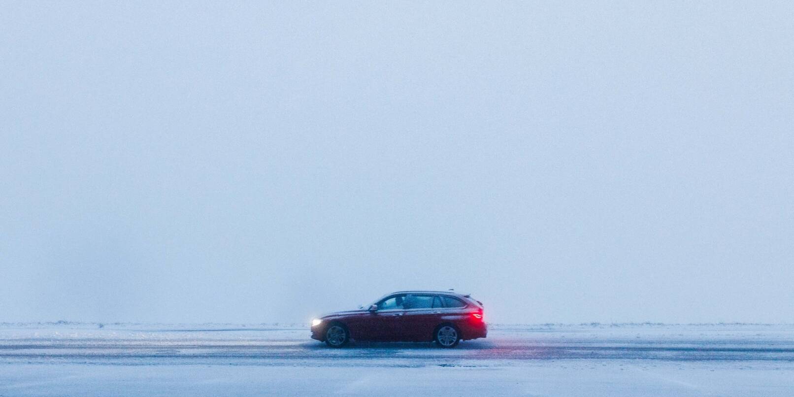 Ein Auto fährt bei dichtem Nebel über eine schneebedeckte Straße.