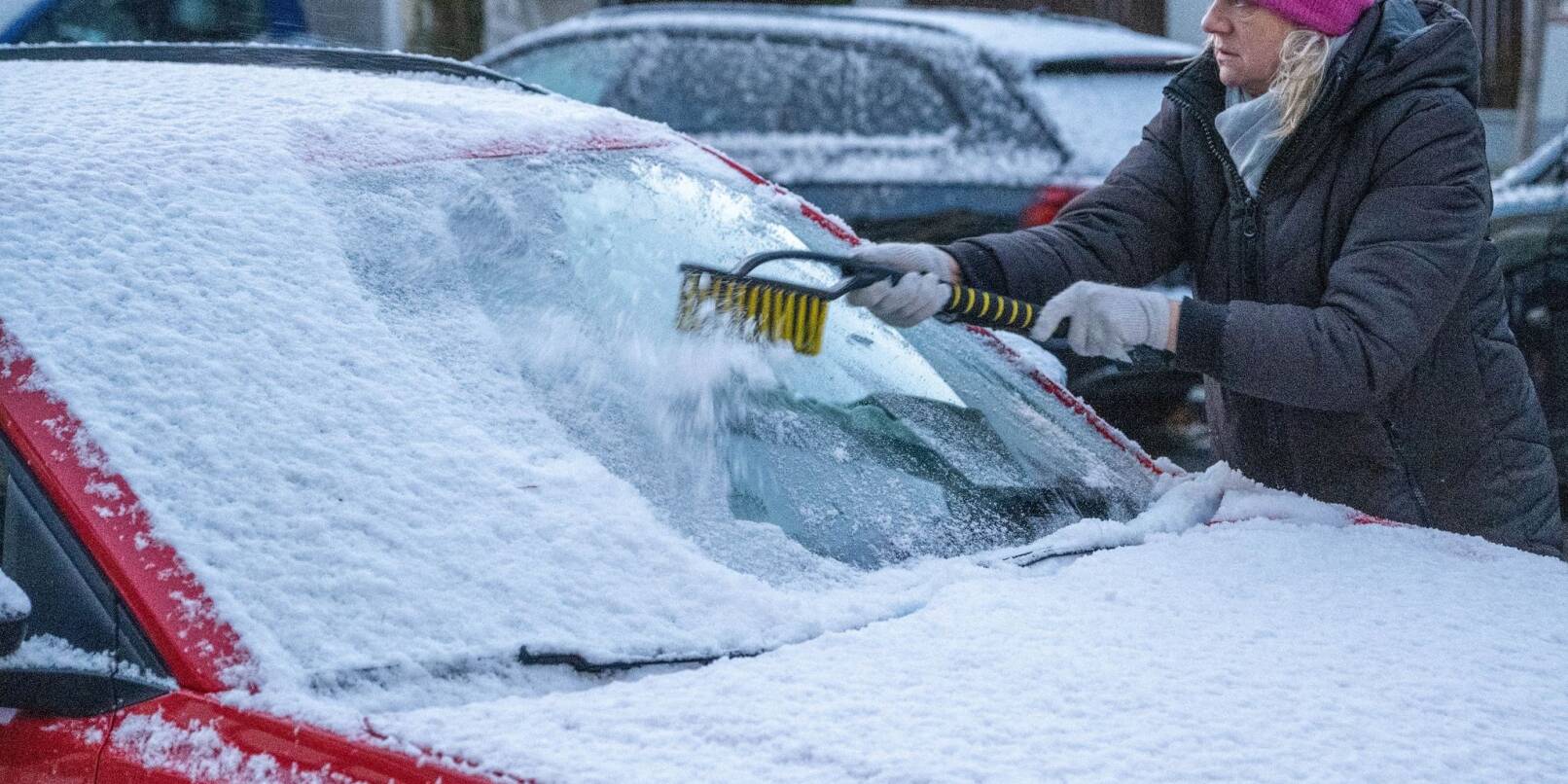 Eine Frau in München befreit am frühen Morgen ein Auto von Schnee und Eis. Auch in den kommenden Tagen soll es winterlich bleiben.