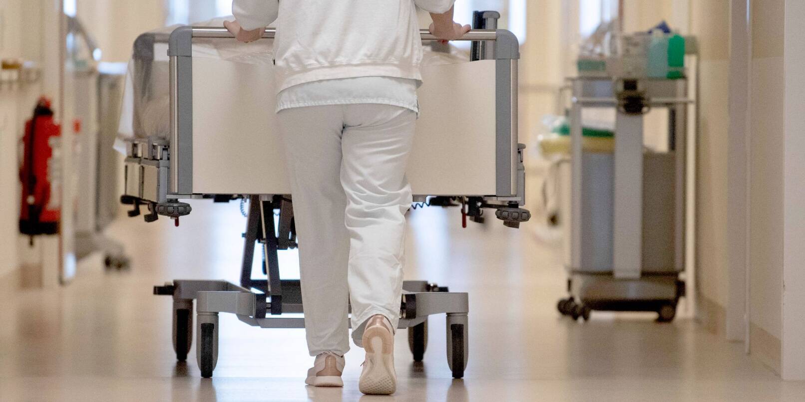 Eine Krankenpflegerin schiebt ein Krankenbett durch einen Flur.