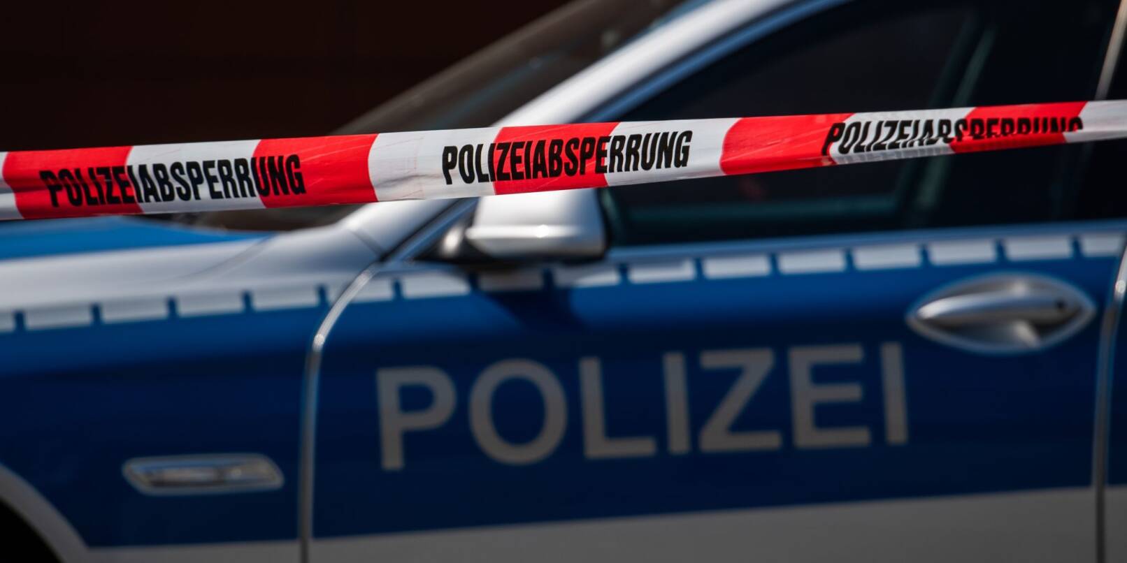 Ein Polizeiauto steht hinter einem Absperrband der Polizei. Ein Polizeiauto steht hinter einem Absperrband der Polizei.