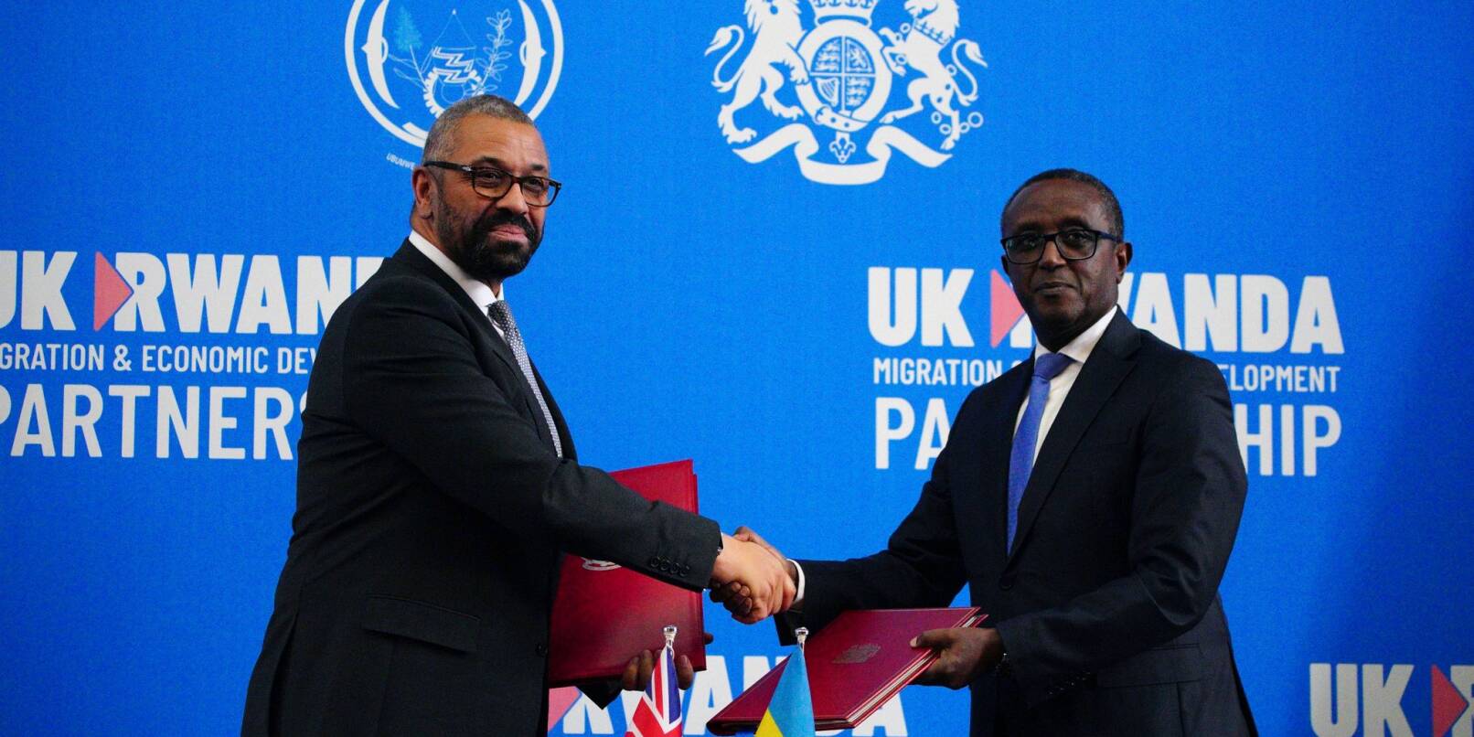 Großbritanniens Innenminister James Cleverly (l) und Vincent Birut, Außenminister von Ruanda, schütteln sich die Hände. Mit dem neuen Vertrag will die britische Regierung Asylsuchende künftig in das ostafrikanische Land abschieben.