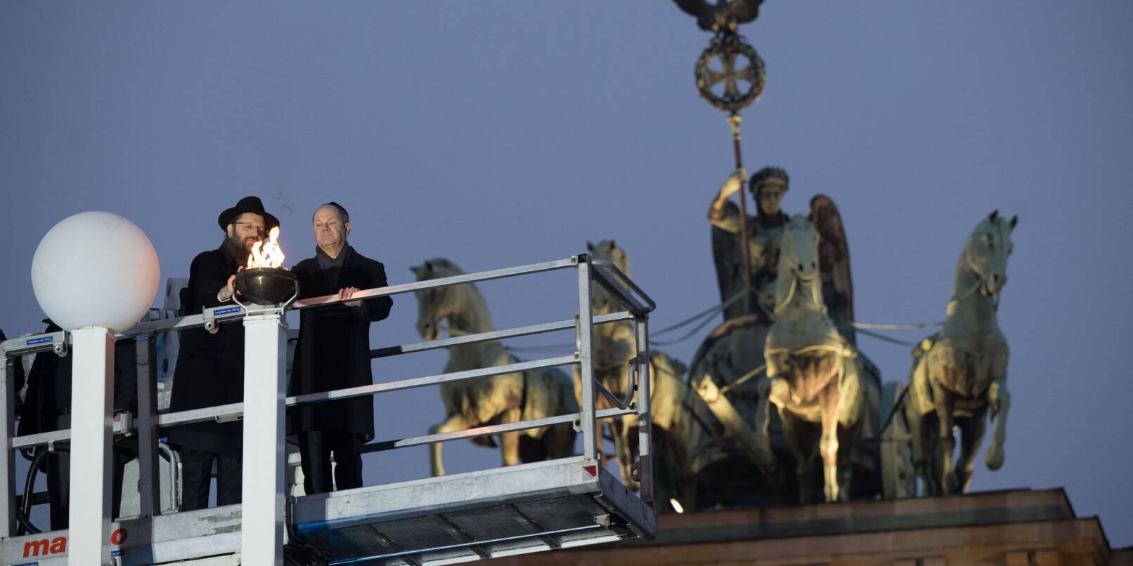 Rabbiner Yehuda Teichtal (l.) und Bundeskanzler Olaf Scholz zünden beim traditionellen zentralen Chanukka-Lichterzünden am Brandenburger Tor in Berlin ein Licht an.