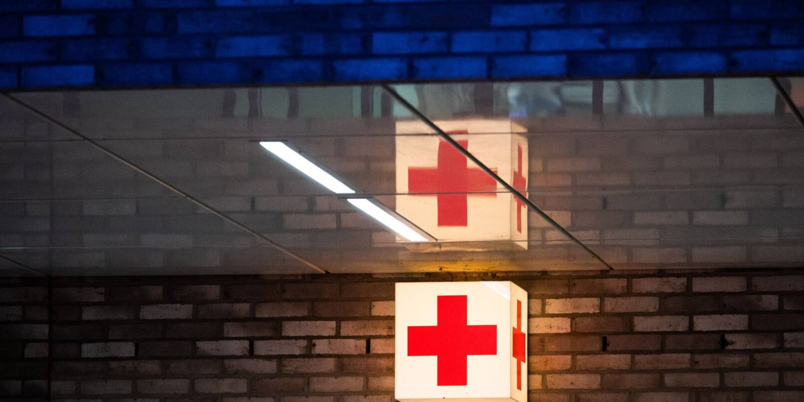Ein Leuchtkasten mit einem roten Kreuz hängt vor der Notaufnahme eines Krankenhauses.