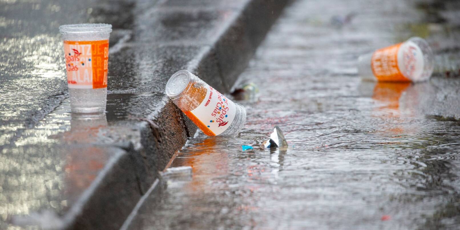Leere Plastikbecher liegen bei strömenden Regen am Straßenrand.