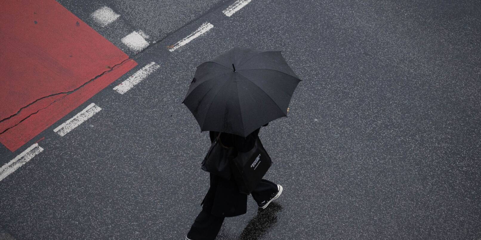 Mit einem Schirm schützt sich eine Passantin in Frankfurt vor dem strömenden Regen.