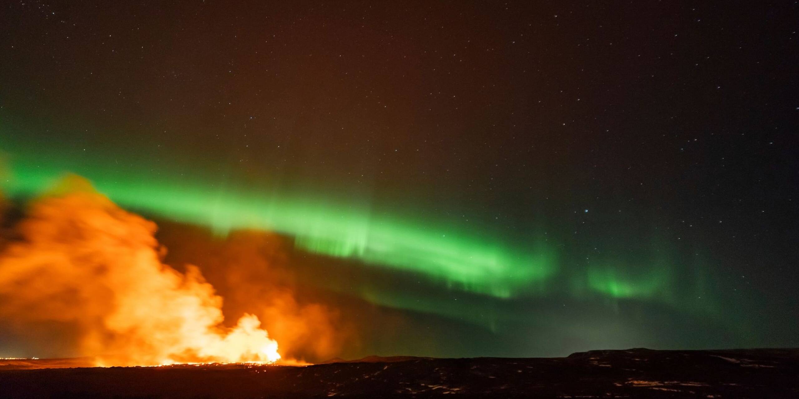Rauch steigt vom Ausbruchsgebiet eines Vulkans im Südwesten Islands auf, während Polarlichter am Himmel erscheinen.