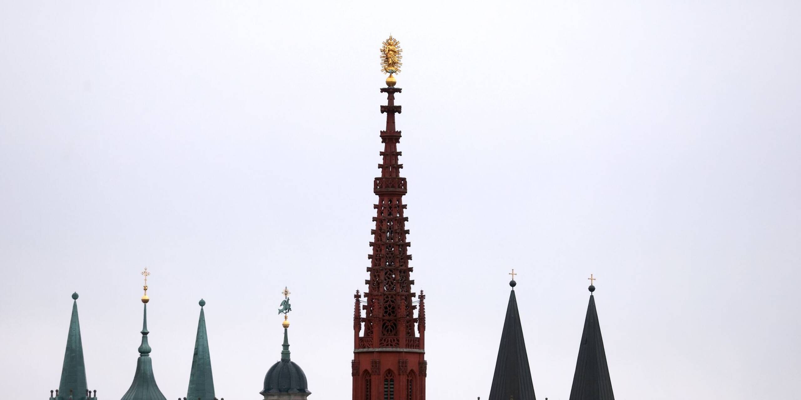 Karfreitag in Bayern: Die Türme des Doms, der Neumünsterkirche und der Marienkapelle zeichnen sich in Würzburg vor dem bewölktem Himmel ab.