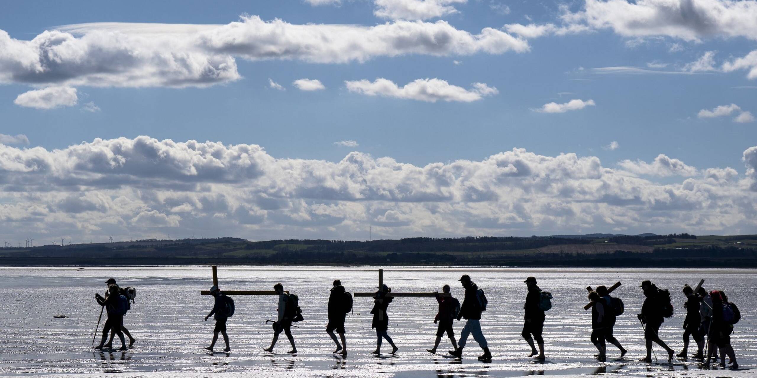 Pilger tragen bei Ebbe Holzkreuze über den Sand zur Heiligen Insel Lindisfarne im englischen Northumberland.