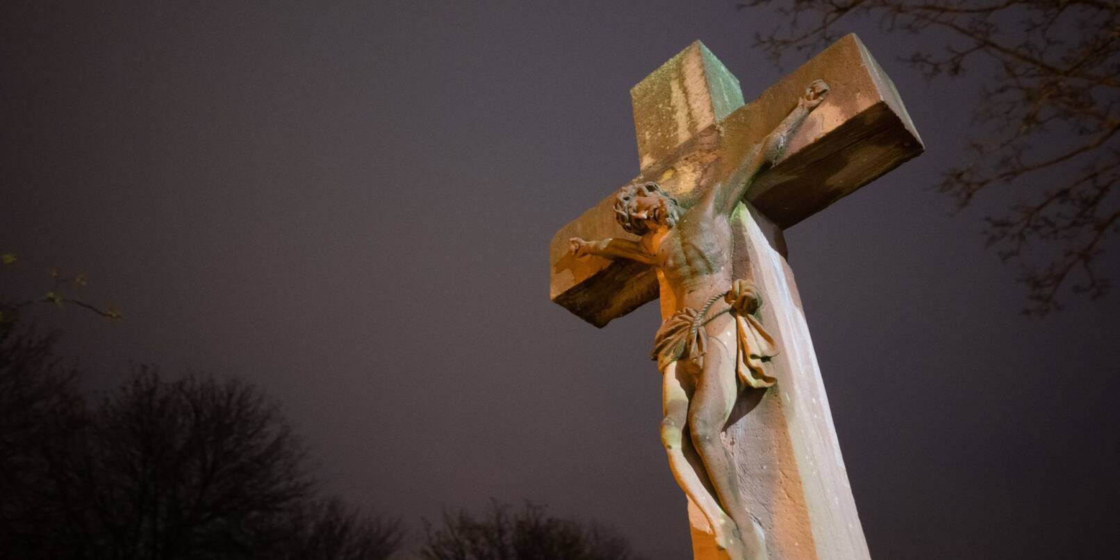 Eine Steinkreuz mit Jesusfigur wird von einem Licht angeleuchtet. Am Karfreitag gedenken Christen an das Leid und das Sterbens Jesu Christi am Kreuz.