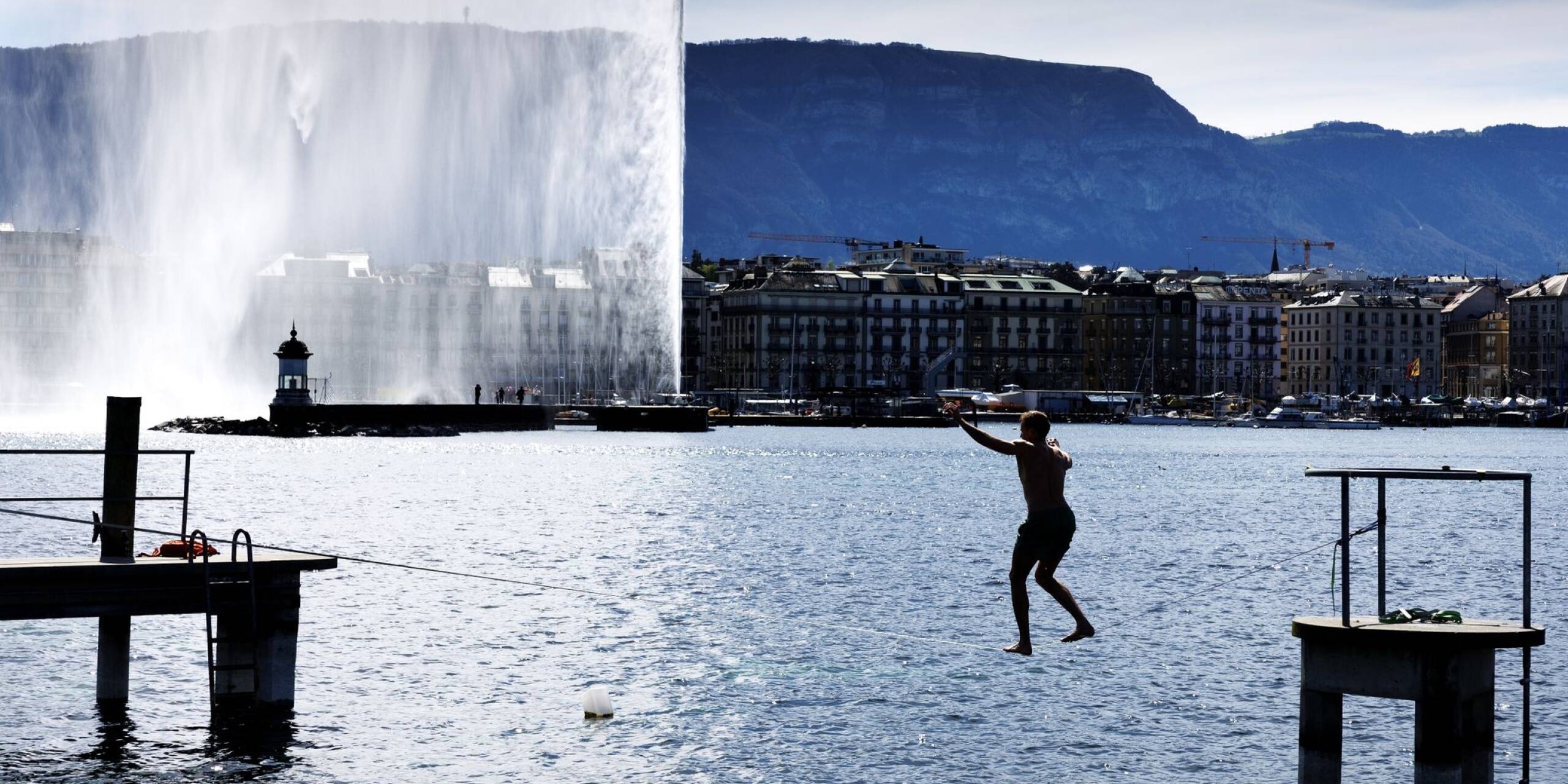 Ein Mann nutzt das Frühlingswetter und balanciert bei strahlendem Sonnenschein auf einer Slackline über den Genfer See.