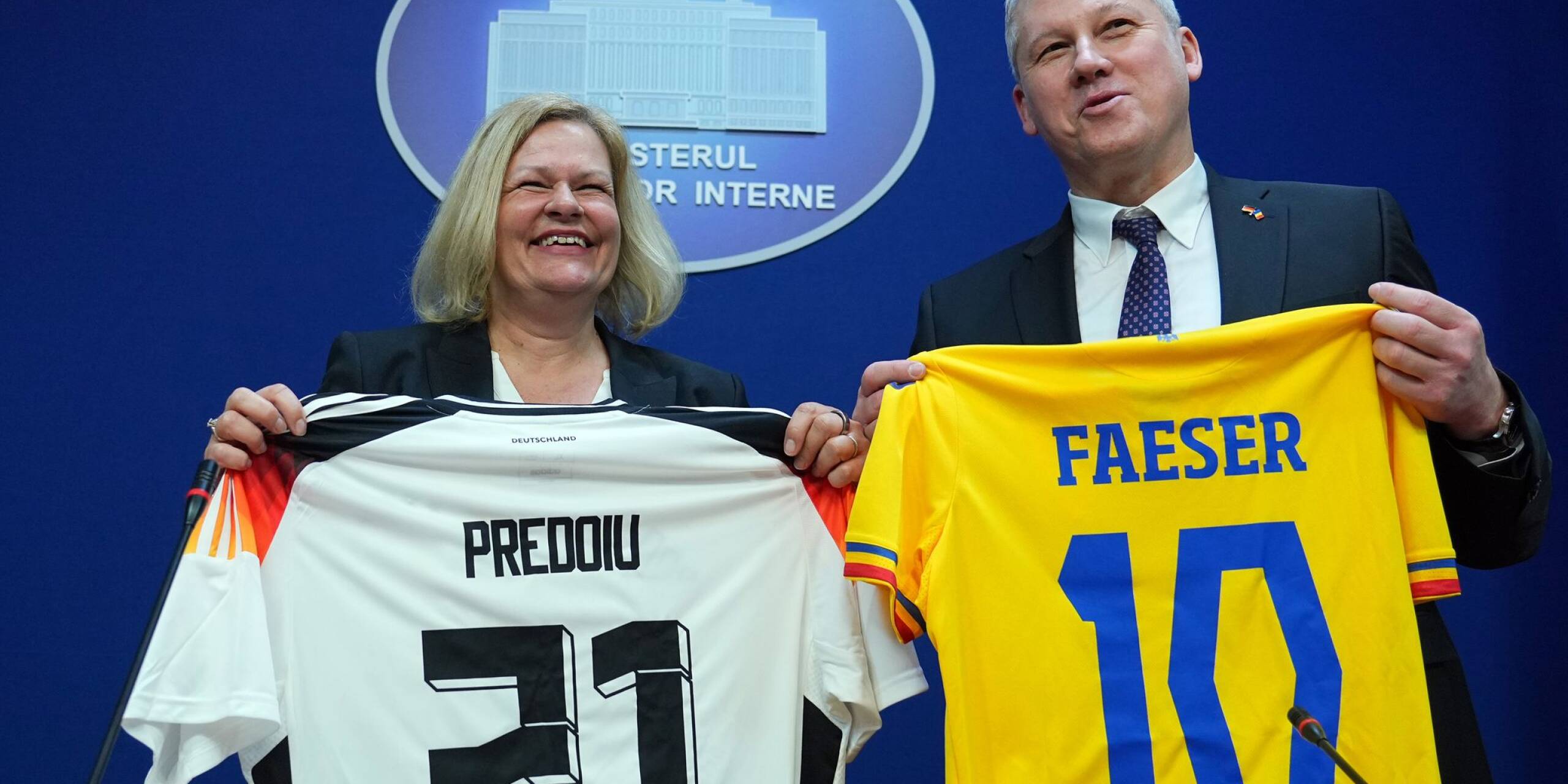 Bundesinnenministerin Nancy Faeser und ihr rumänischer Amtskollege Marian Catalin Predoiu halten nach einer gemeinsamen Pressekonferenz Trikots der jeweiligen Fussball-Nationalmannschaft in den Händen.