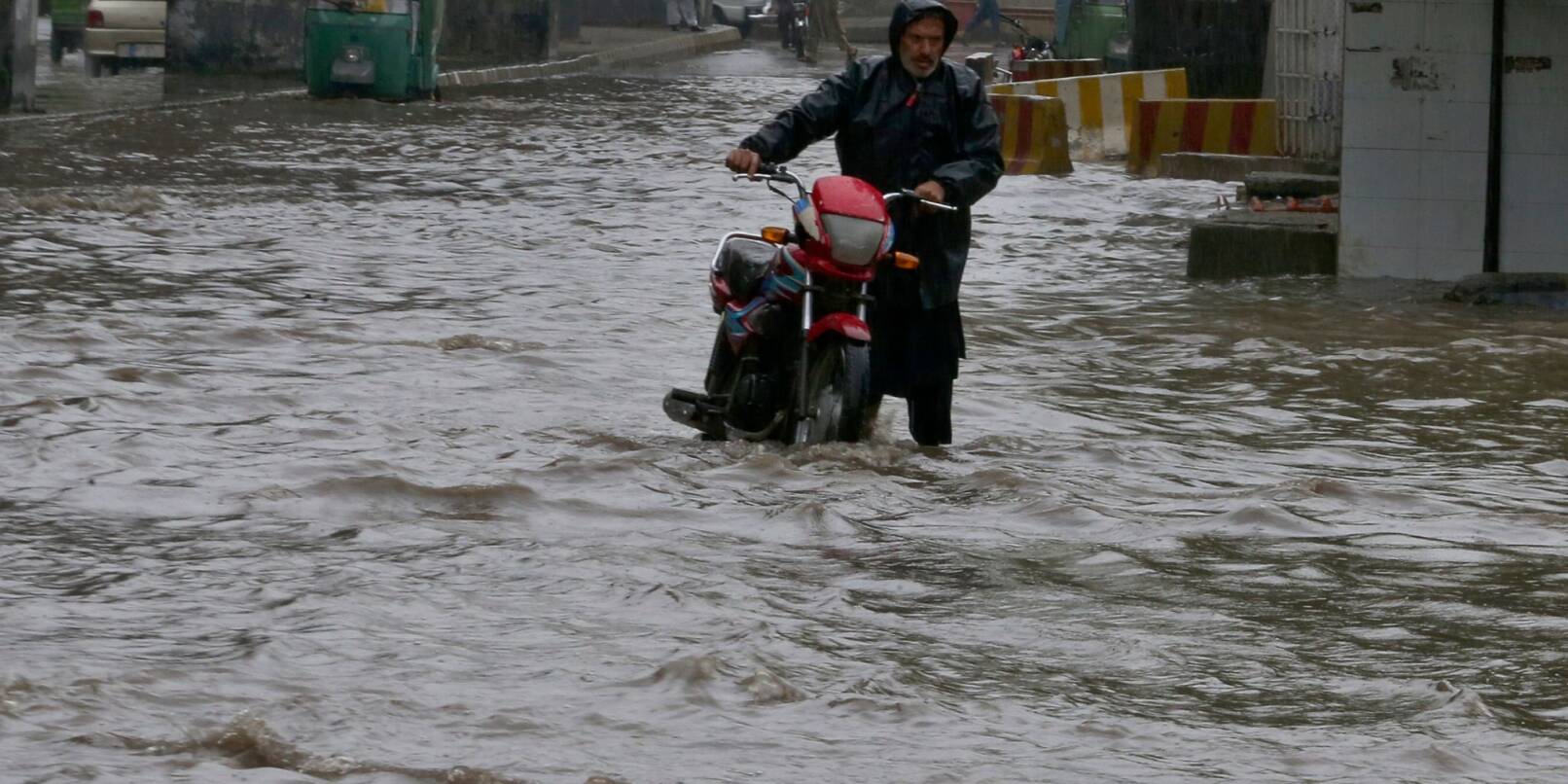 Ein Pakistaner watet nach starken Regenfällen mit seinem Motorrad durch eine überschwemmte Straße in Peschawar.
