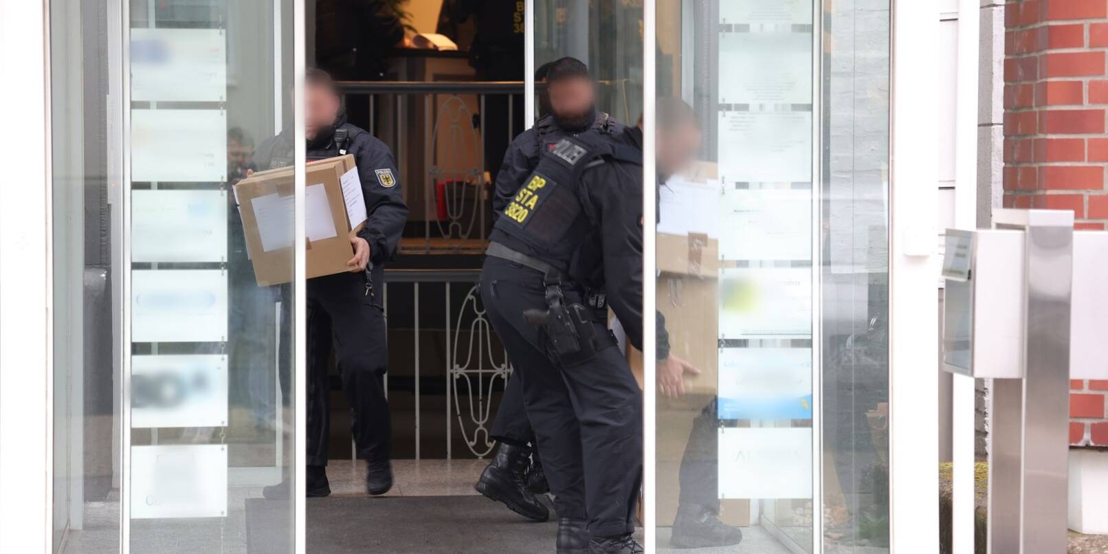 Polizeibeamte tragen in Kartons sichergestelltes Material aus einem Gebäude.