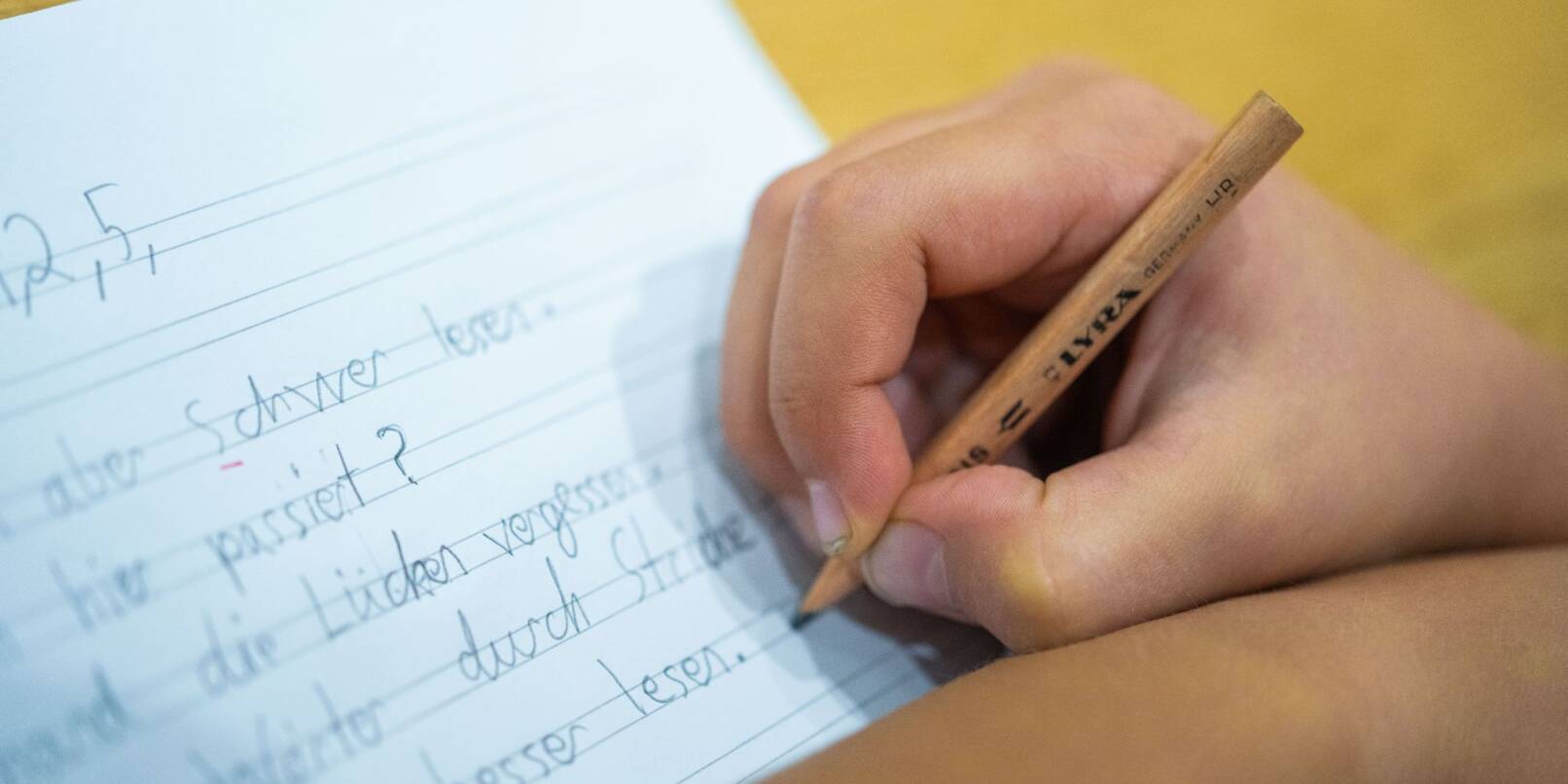 Ein Grundschüler schreibt mit Bleistift in sein Heft.