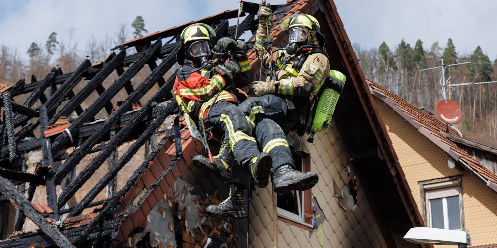 Zwei Feuerwehrleute werden mit Hilfe einer Drehleiter aus dem ausgebrannten Dachstuhl herausgehoben.