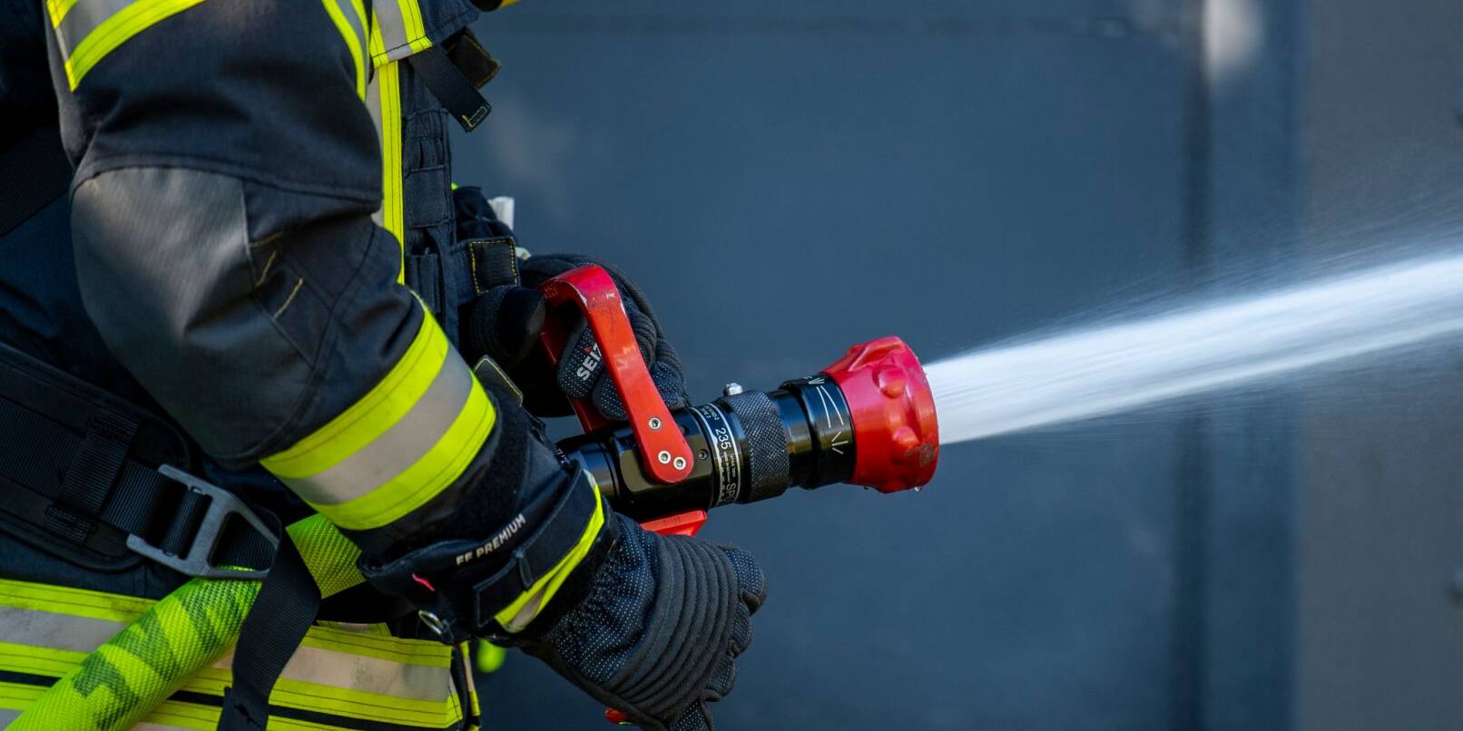 Ein Mitglied der Feuerwehr spritzt aus einem Schlauch mit Wasser. Ein Mitglied der Feuerwehr spritzt aus einem Schlauch mit Wasser.