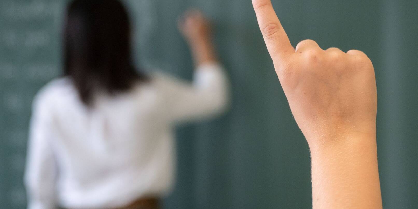 Ein Schüler meldet sich, während die Lehrerin an die Tafel schreibt.
