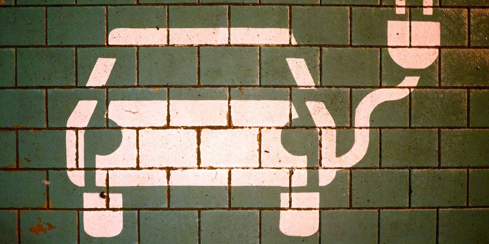 Ein Symbol markiert einen Parkplatz mit einer öffentlichen Ladesäule für Elektroautos an einem Einkaufszentrum. Ein Symbol markiert einen Parkplatz mit einer öffentlichen Ladesäule für Elektroautos an einem Einkaufszentrum.