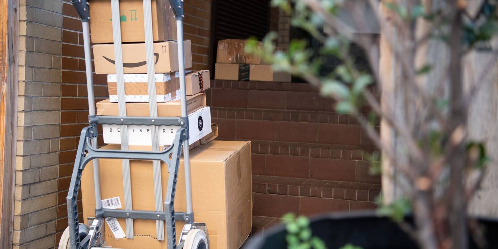 Pakete stehen auf einer Karre, während ein Paketzusteller Pakete ausliefert. Pakete stehen auf einer Karre, während ein Paketzusteller Pakete ausliefert.