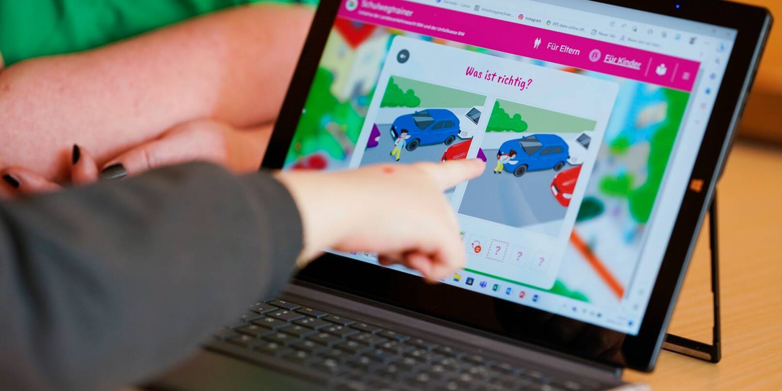 Ein Kindergartenkind zeigt auf eine auf einem Tablet geöffnete Internetseite des «Schulwegtrainers».
