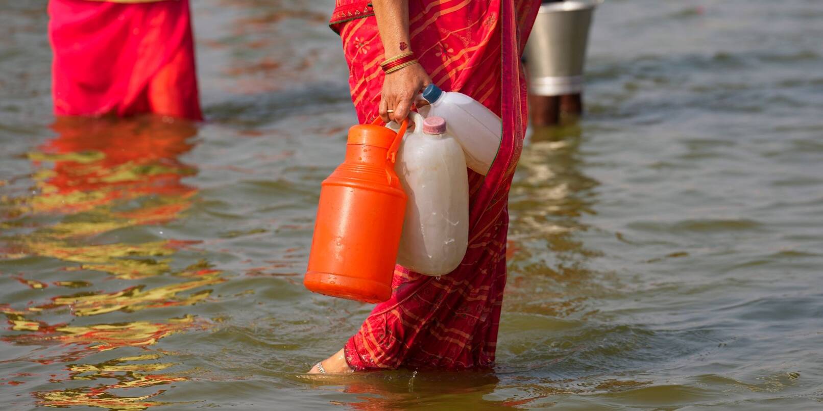 Eine Hinduistin geht nach dem Wasserholen mit Kunststoffkanistern im Sangam, dem Zusammenfluss des Ganges und Yamuna.
