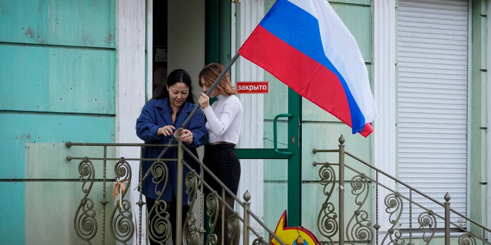 Frauen hängen im September 2022 eine russische Flagge in ihrem Geschäft in Luhansk auf.