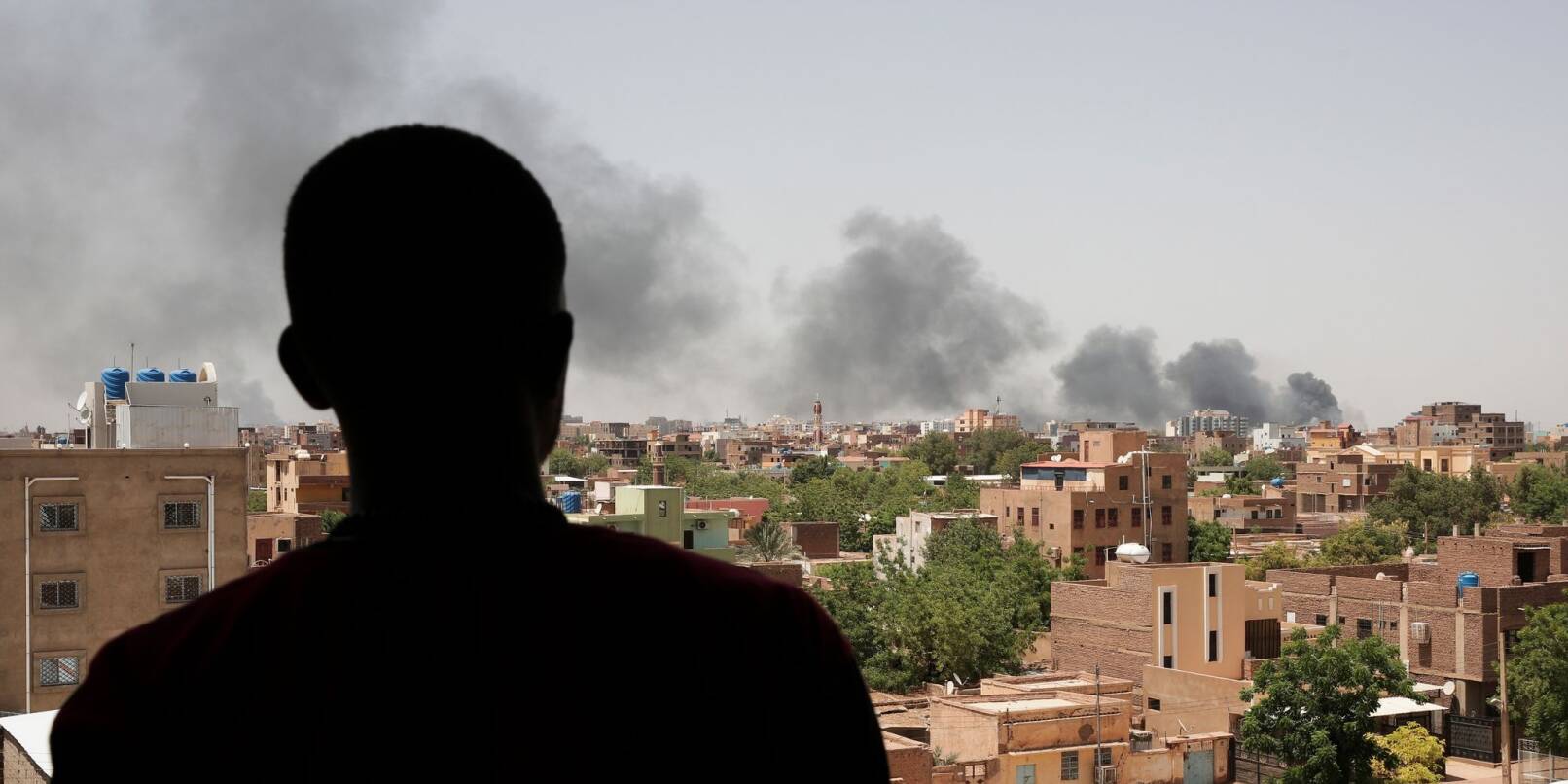 Ein Mann blickt auf die Stadt Khartum, wo infolge von Kämpfen schwarzer Rauch aufsteigt.
