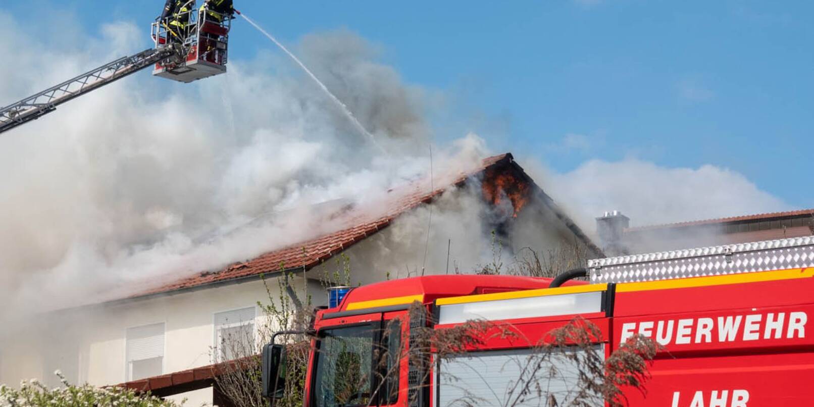 Einsatzkräfter der Feuerwehr löschen von einer Drehleiter aus einen Brand in einem Haus.