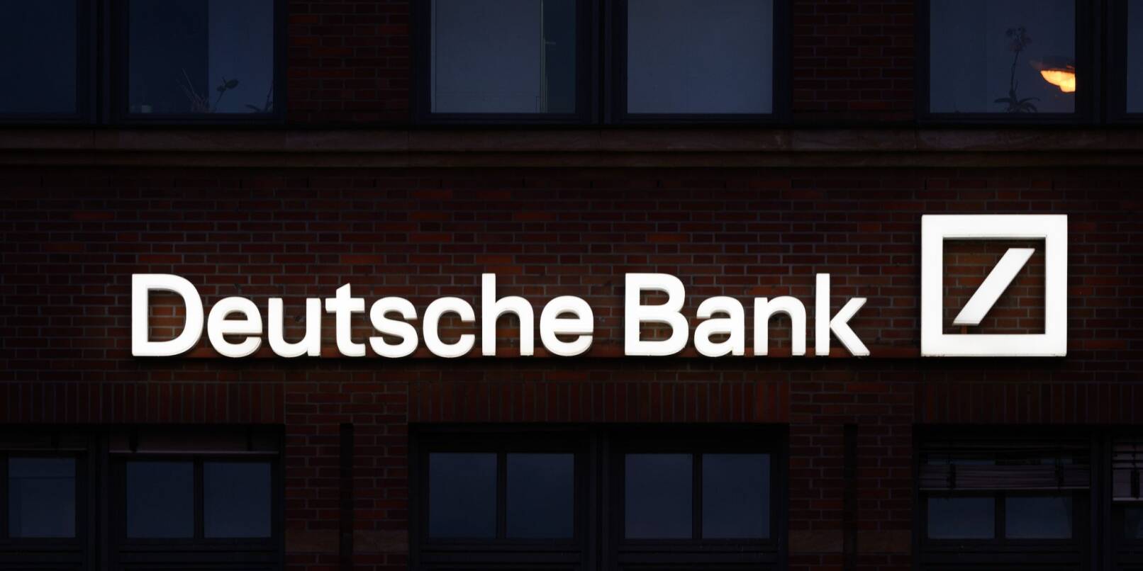 Das Logo der Deutschen Bank leuchtet an einer Filiale.